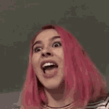 a woman with pink hair is smiling and making a funny face .