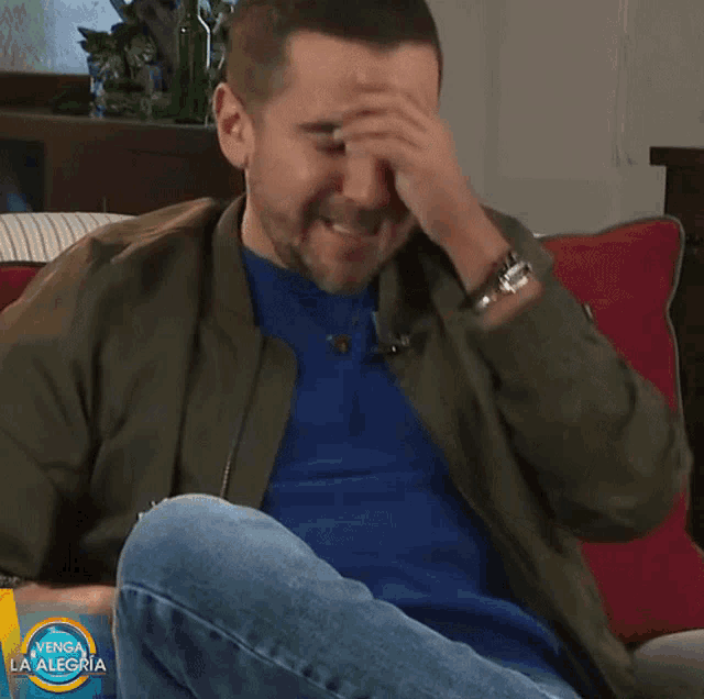 a man sitting on a couch covering his face with his hand and a sign that says venga la alegria
