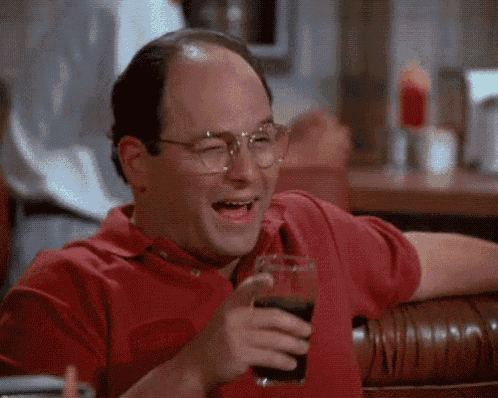 a man in a red shirt and glasses is holding a glass of soda and laughing .