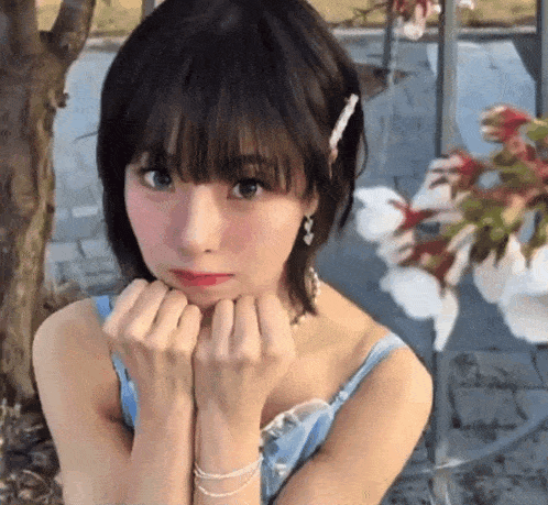a woman in a blue tank top holds her hands to her chin