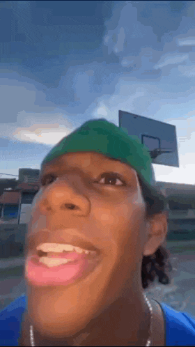 a man wearing a green hat is making a funny face in front of a basketball hoop .