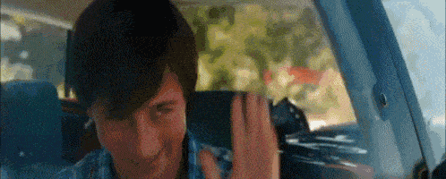 a young man is sitting in the back seat of a car waving at the camera .