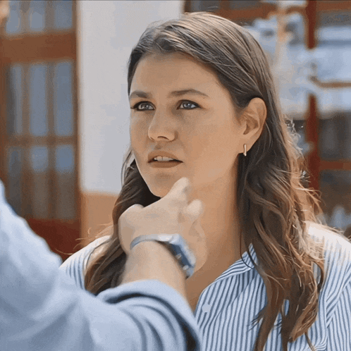 a woman in a blue and white striped shirt has her hand on her chin