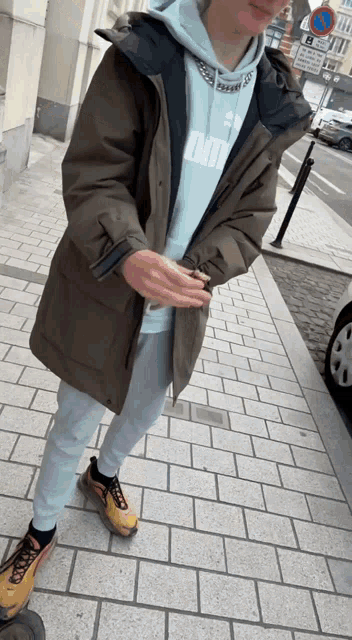 a man wearing a hoodie that says omi stands on a sidewalk