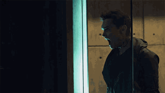 a man with a tattoo on his arm is screaming behind a glass door