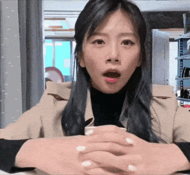 a woman is sitting at a table with her hands folded in front of her face