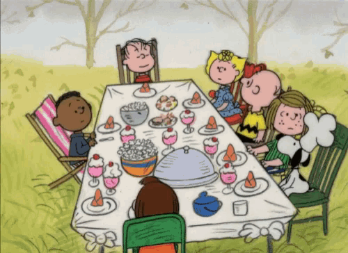a group of peanuts characters are sitting around a table with food on it