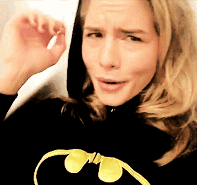 a woman is wearing a black hoodie with a yellow batman logo on it