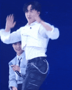 a man in a white shirt is waving while another man holds a microphone behind him