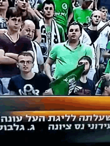 a man in a green shirt is holding a green flag in front of a crowd of people