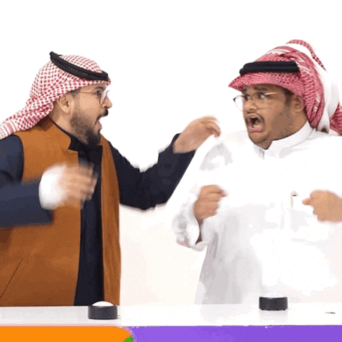 a man in a red and white head scarf is talking to another man in a white shirt