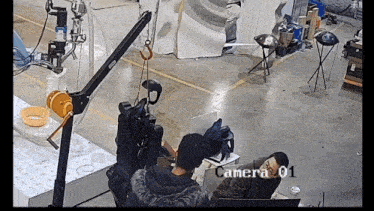 a man sits at a desk in front of a camera that says camera 01 on the bottom
