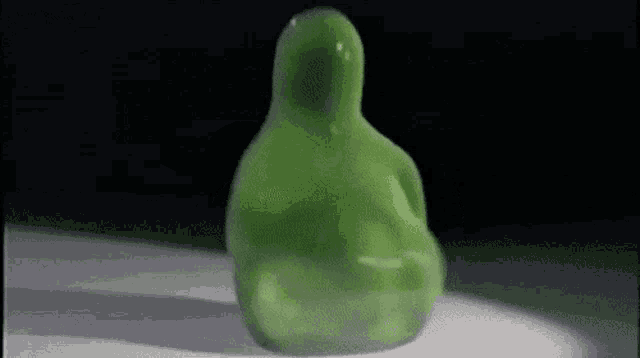 a green figurine is sitting on a white surface .
