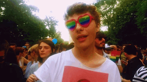 a man wearing rainbow heart shaped sunglasses is standing in a crowd