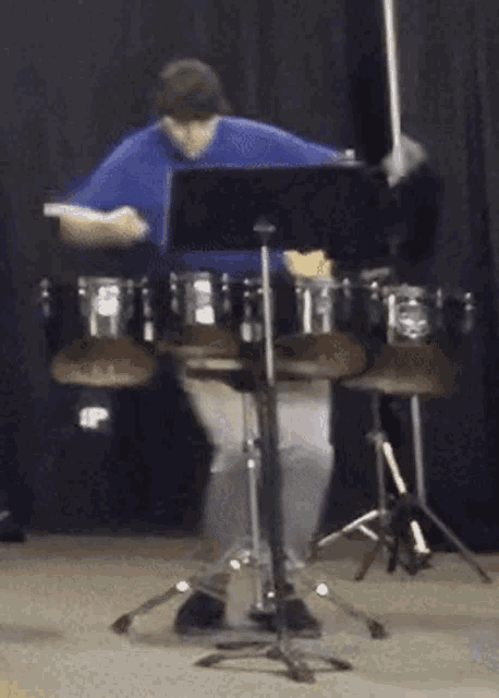 a man in a blue shirt is playing drums in a dark room