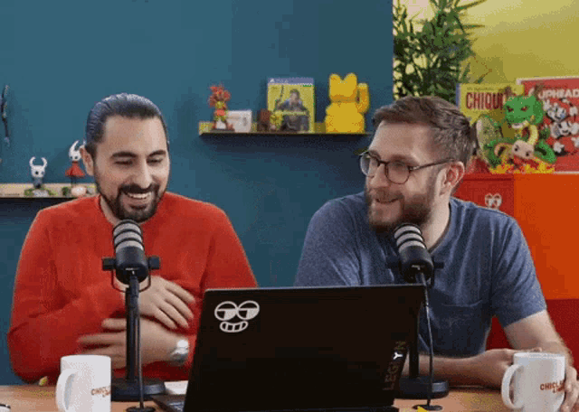 two men are sitting in front of a laptop with a legion logo on it