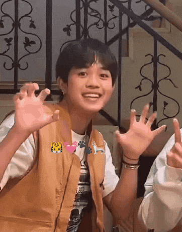 a young boy wearing a brown vest is making a funny face with his hands in the air .