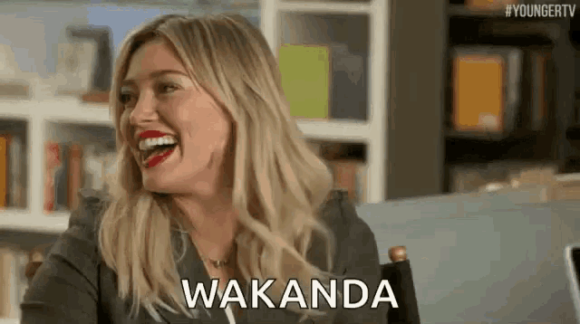 a woman is laughing while sitting in a chair with the word wakanda written on her face .