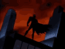 a silhouette of batman standing on top of a building with a red sky in the background