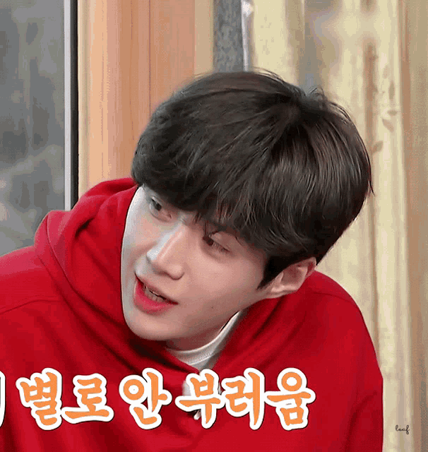 a young man wearing a red hoodie with chinese writing behind him