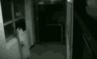 a man in a suit and tie is walking down a hallway with a ghost behind him .