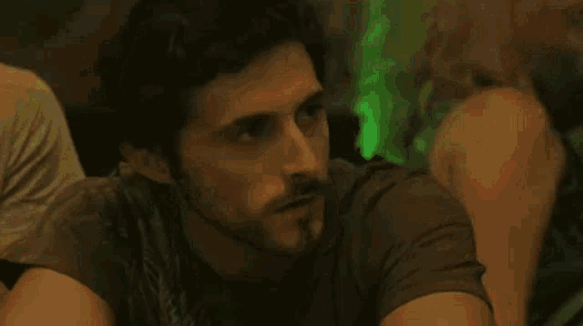 a man with a beard is sitting in a dark room with a green background .