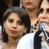 a woman is holding a microphone in her mouth while sitting in a crowd .