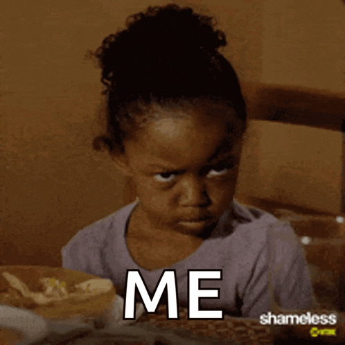 a little girl is sitting at a table with a plate of food and the words me written on her face