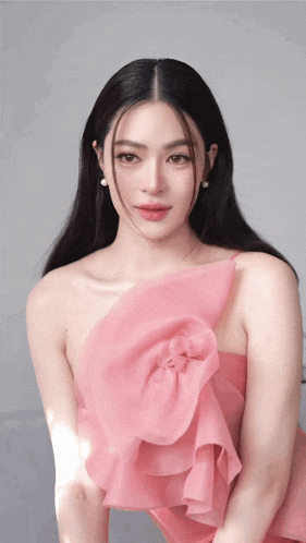 a woman in a pink dress with a flower on the front looks at the camera