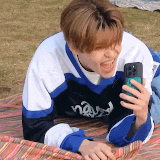 a young man is laying on a blanket while holding a cell phone and laughing .