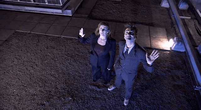 a man and a woman standing on a roof with their hands up