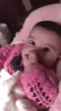 a baby is laying on a bed with a pink teddy bear .