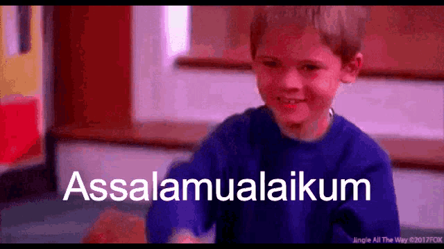 a young boy is smiling in front of a sign that says assalaamualaikum