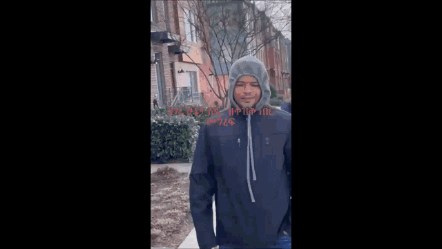 a man in a hooded jacket is walking down the sidewalk next to another man .