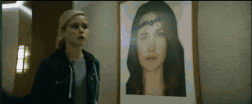 a woman stands in front of a framed portrait of a woman