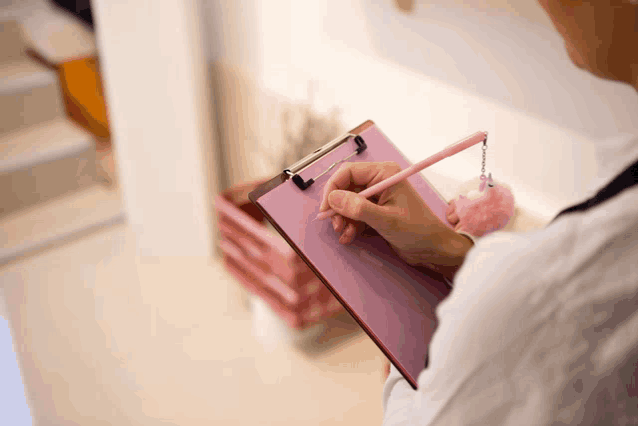 a person writing on a clipboard with a pink pencil