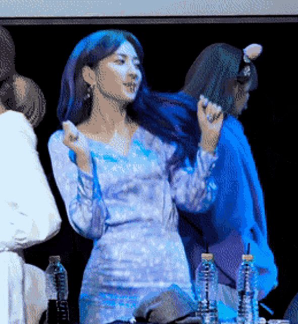 a woman in a blue dress is dancing in front of bottles of water