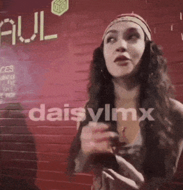 a woman is standing in front of a red brick wall with the word daisylmx written on it .