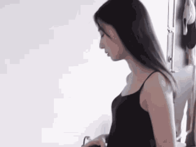 a woman in a black tank top is standing in front of a white wall in a room .