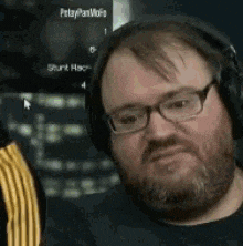 a man with a beard and glasses is wearing headphones and making a face .