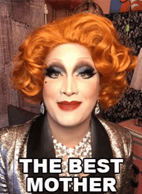 a drag queen is wearing a wig and earrings and says " the best mother "