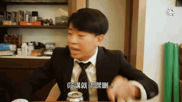 a man in a suit and tie sits at a table with a can of beer