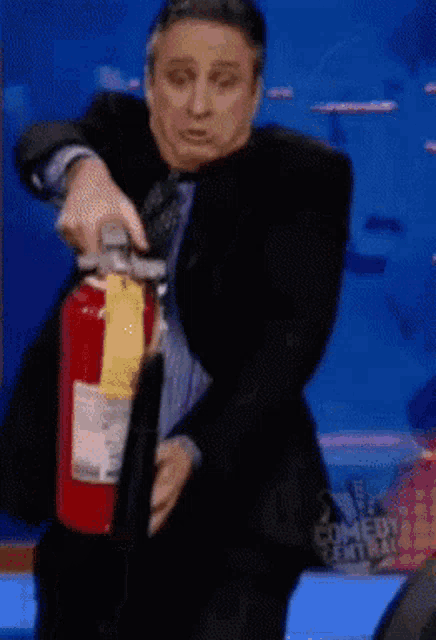 a man in a suit is holding a fire extinguisher in front of a sign that says comedy central