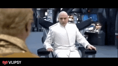 a bald man in a white suit is sitting in a chair