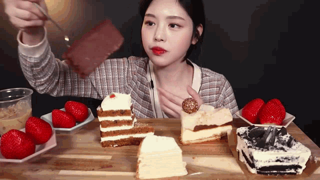 a woman is eating a slice of cake with strawberries on the side