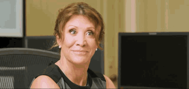 a woman sitting in front of a computer monitor making a face