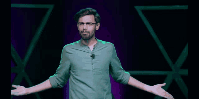 a man wearing glasses and a green shirt is standing with his arms outstretched on a stage