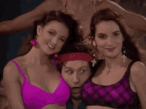 a man with a red bandana on his head is surrounded by two women in pink bikinis .