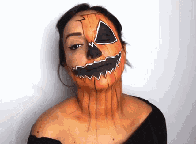 a woman has her face painted to look like a pumpkin .