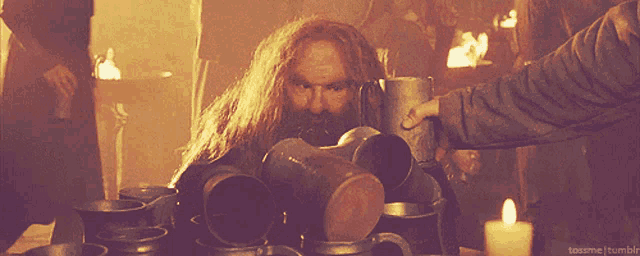 a man with a beard stands in front of a pile of mugs